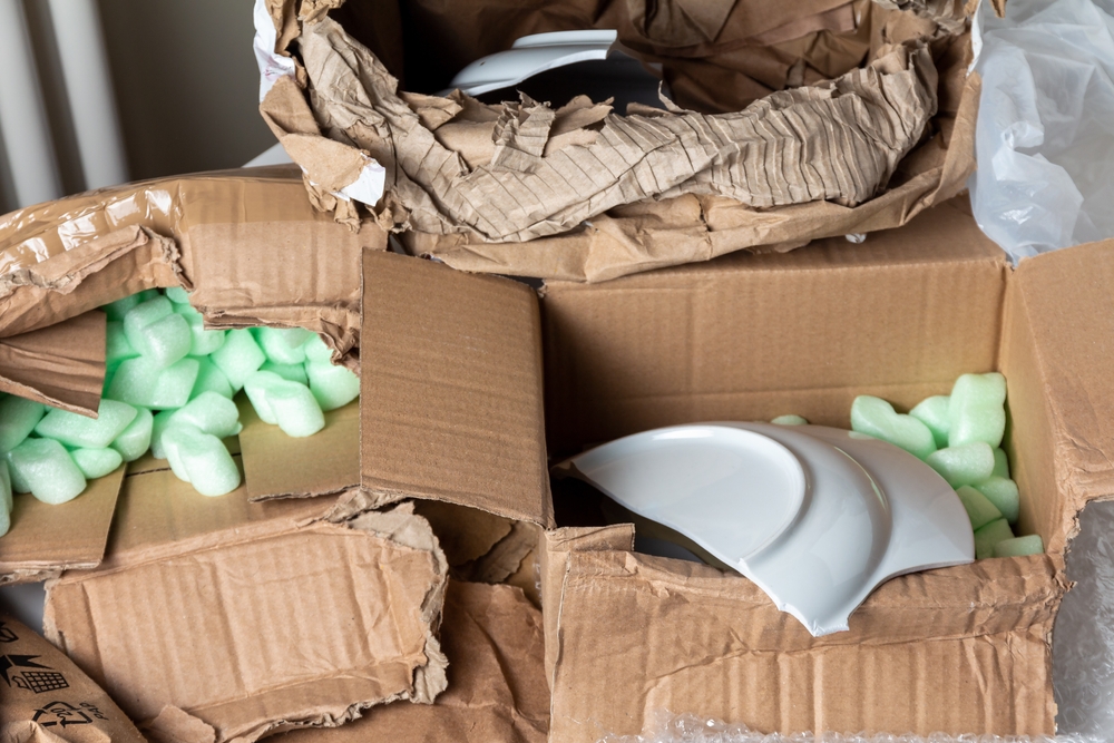 Various boxes ripped and stacked filled with packing peanuts and a broken plates.