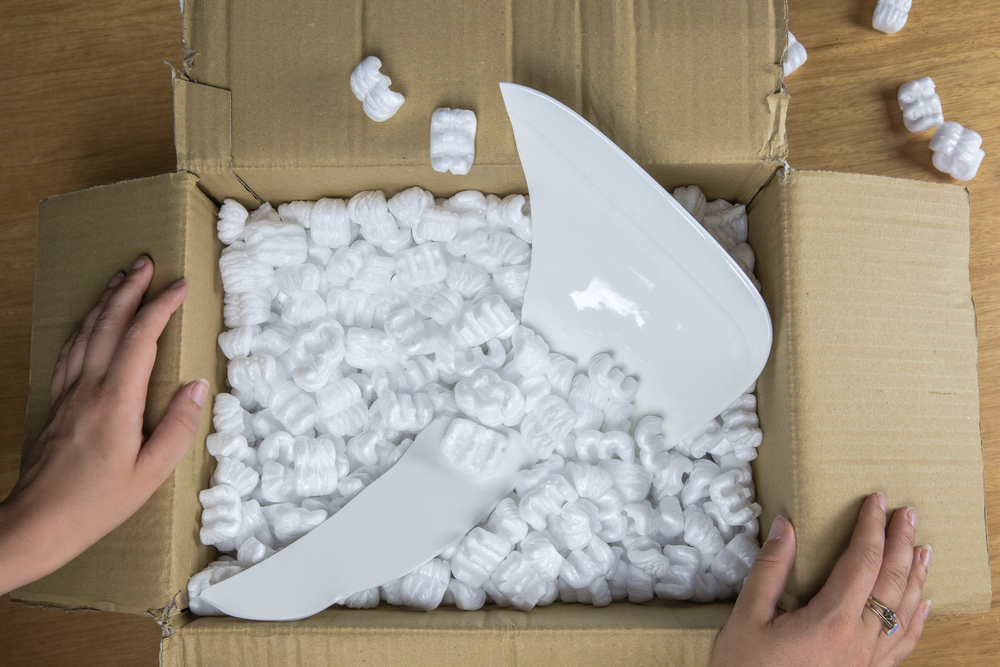 A woman's hand holding open a box filled with packing peanuts and a broken plate. 