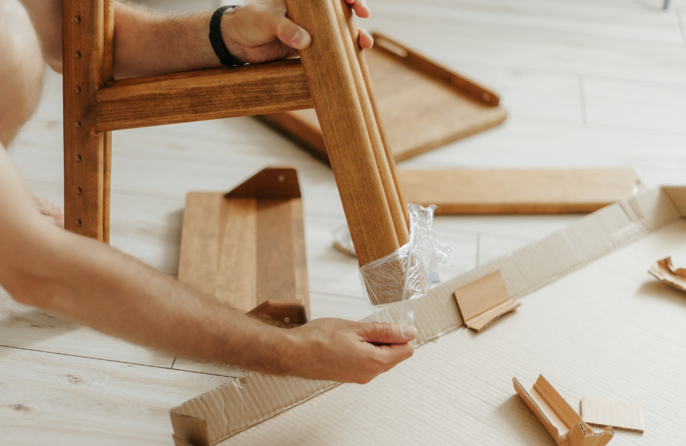 Two hands removing plastic wrap from a piece of furniture. 