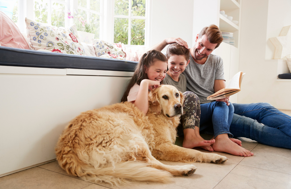 A father and his two children sitting on the ground with their golden retriever dog. They are all smiling and happy.