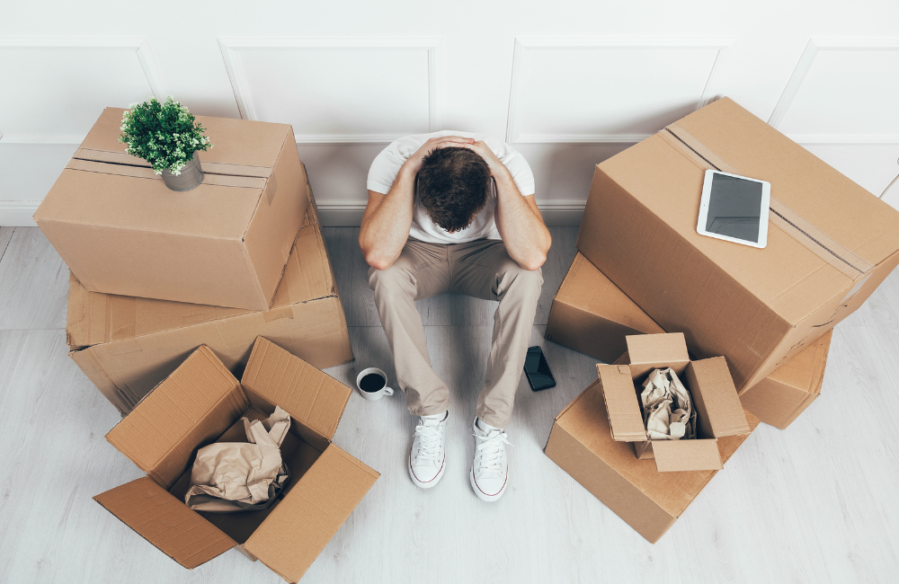 A man surrounded by moving boxes with his head on his knees stressed about moving. 